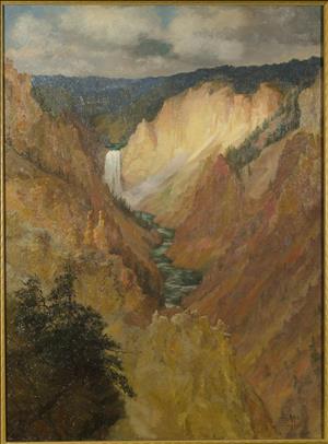 Landscape of waterfall flowing into a river at the base of yellow and orange-brown canyon walls, sunlight highlights right side of canyon wall, fir trees in lower left, dark blue mountains in the far distance, gray sky with clouds.